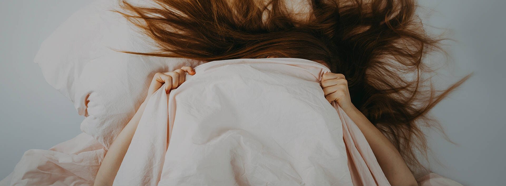 Person zieht sich erschöpft eine helle Decke über den Kopf